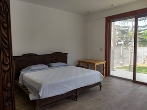 Un dormitorio con una cama, una mesita de noche de madera y un ventanal corredero que da a un balcón.