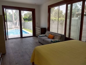 Un dormitorio con cama, sofá y vista a una piscina a través de una puerta corrediza de vidrio.