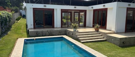 A modern house with a swimming pool, a covered patio, and a well-maintained lawn.