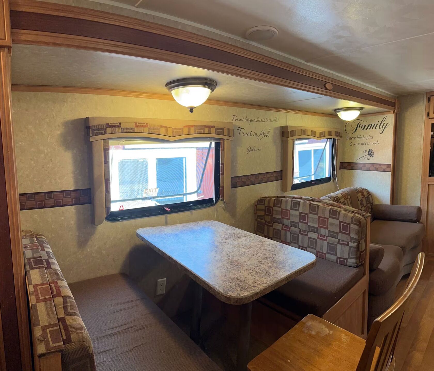 An RV interior with a dining area, two windows, and wall decorations.