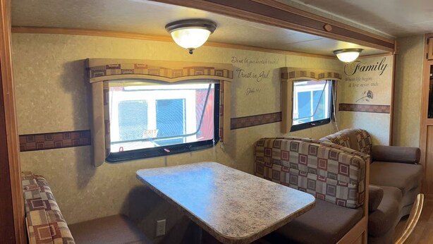 An RV interior with a dining area, two windows, and wall decorations. - Lakefront Escape on Twin Lake Cabin + Trailer (Twin Lake)