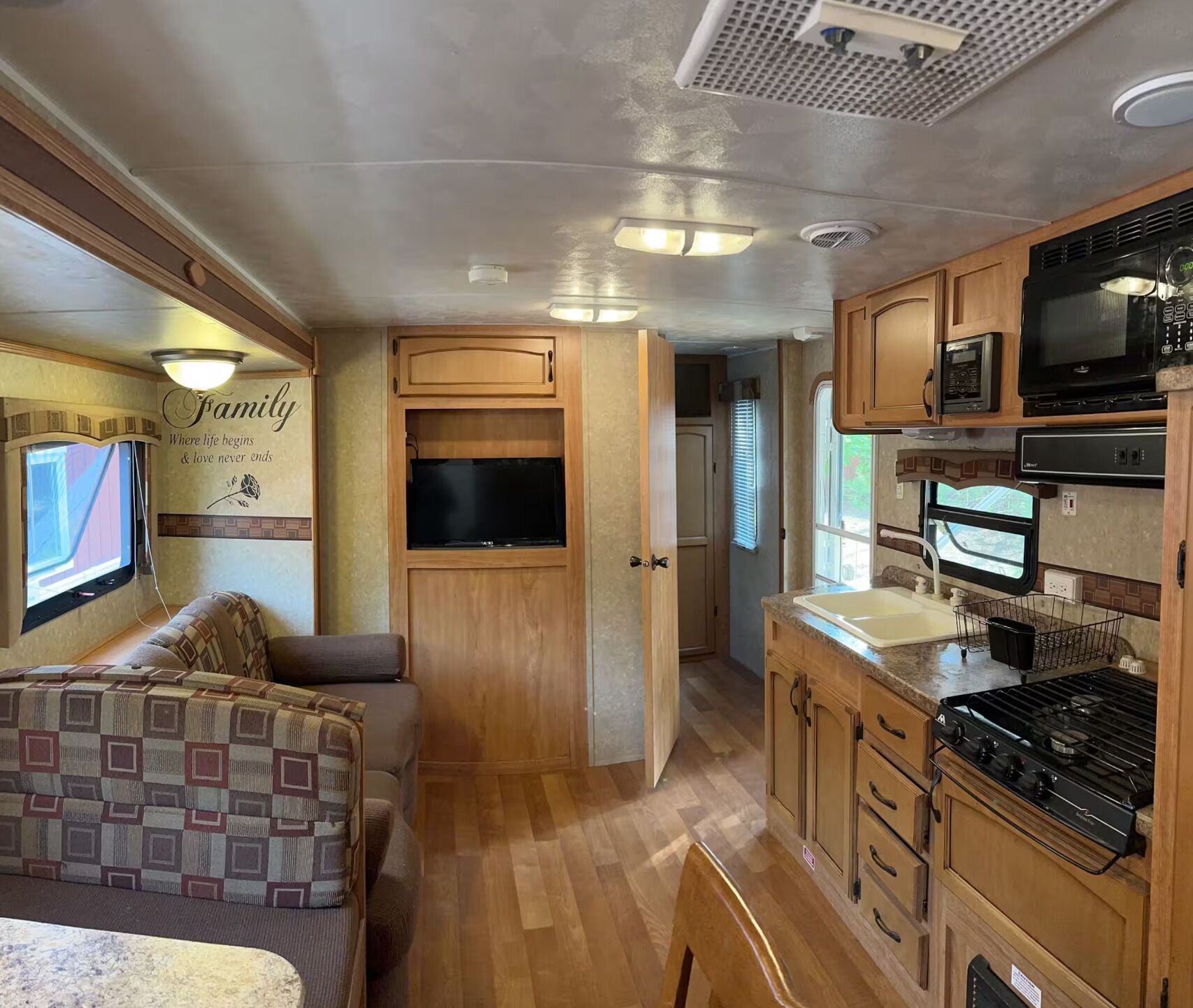 Interior compacto de una autocaravana con kitchenette, zona de estar y televisor.