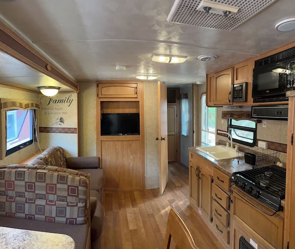 Un intérieur de camping-car compact comprenant un coin cuisine, un espace salon et un téléviseur.