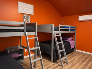 Ein Schlafsaalzimmer mit Etagenbetten, einer Stehleiter, einem kleinen Schreibtisch und einer gerahmten Nachricht an der Wand.