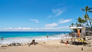 Una playa con una torre de salvavidas, cielo azul despejado y mar tranquilo.