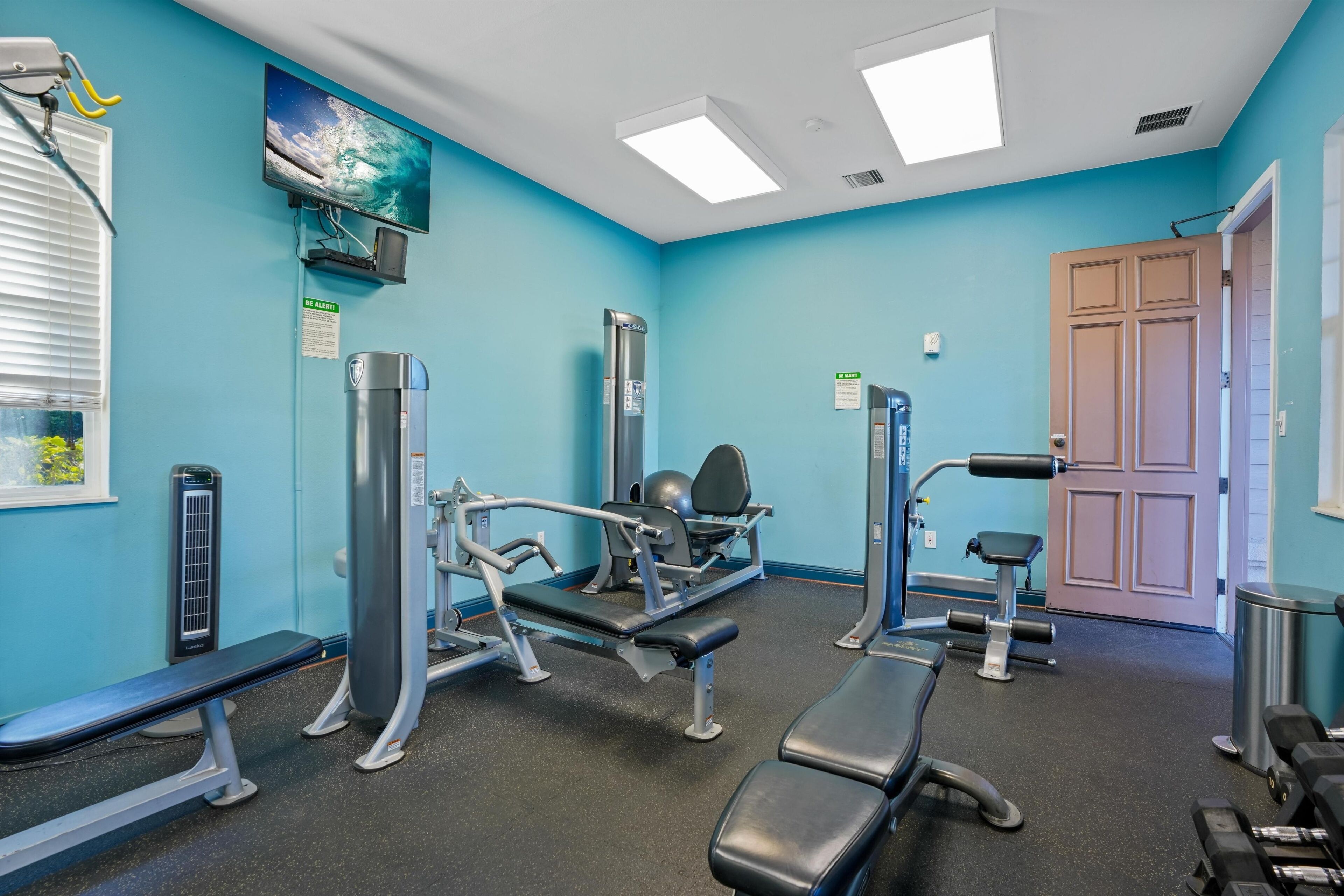 Ein Fitnessraum mit Trainingsgeräten, einem Fernseher und einer Tür.