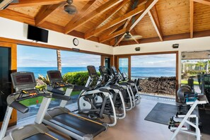 Ein Fitnessraum mit Laufbändern, Ergometer und Rudergerät, mit Blick auf eine malerische Meerlandschaft.