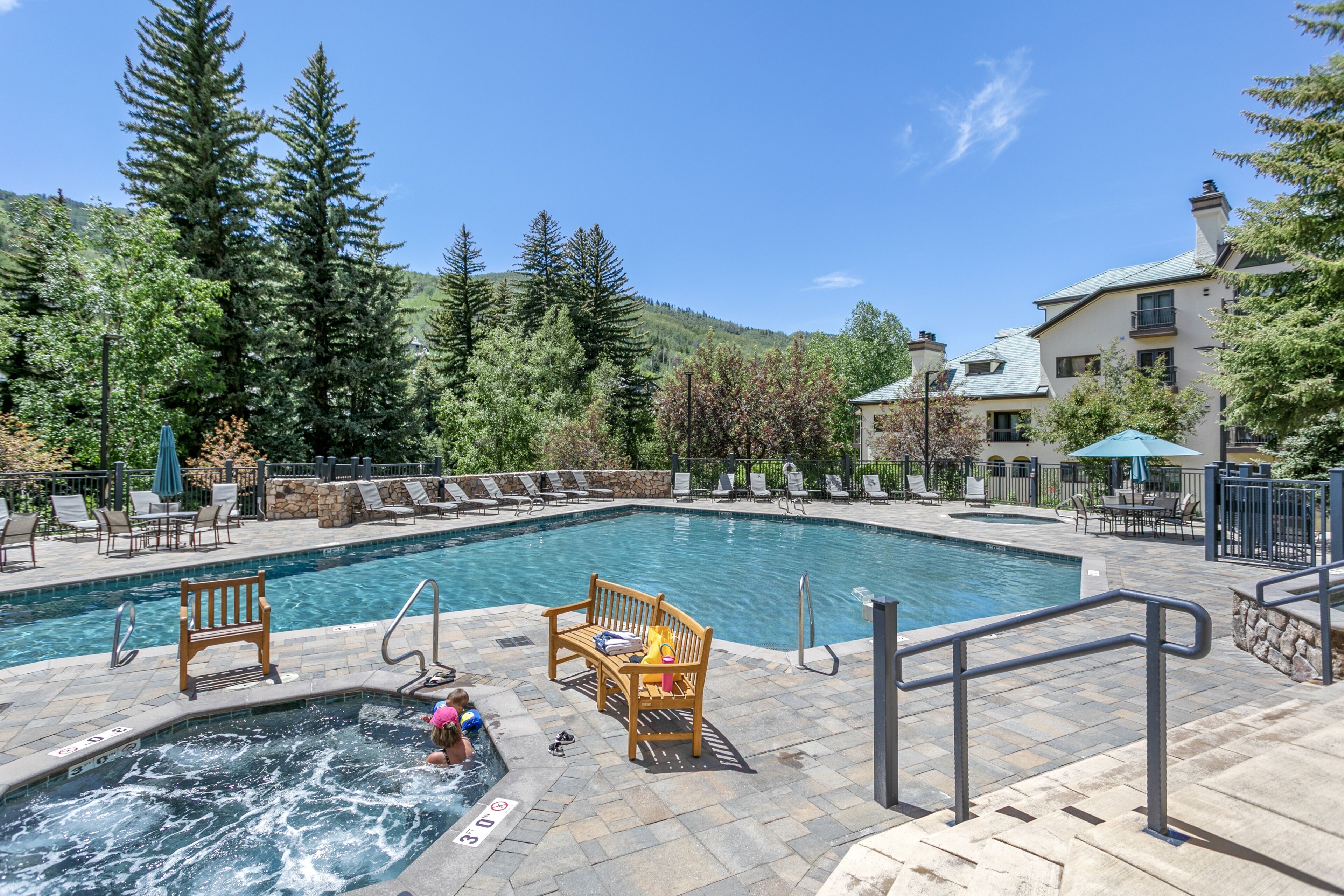 A pool area with a hot tub, lounge chairs, and a stone deck.