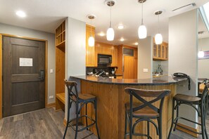 Une cuisine avec des meubles en bois, un micro-ondes noir, un réfrigérateur en acier inoxydable et un coin bar avec des tabourets.