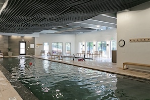 An indoor swimming pool with a bench and chairs, a clock on the wall, and a door leading to another room. - Charter At Beaver Creek E160 2 Bedroom Condo (Avon)