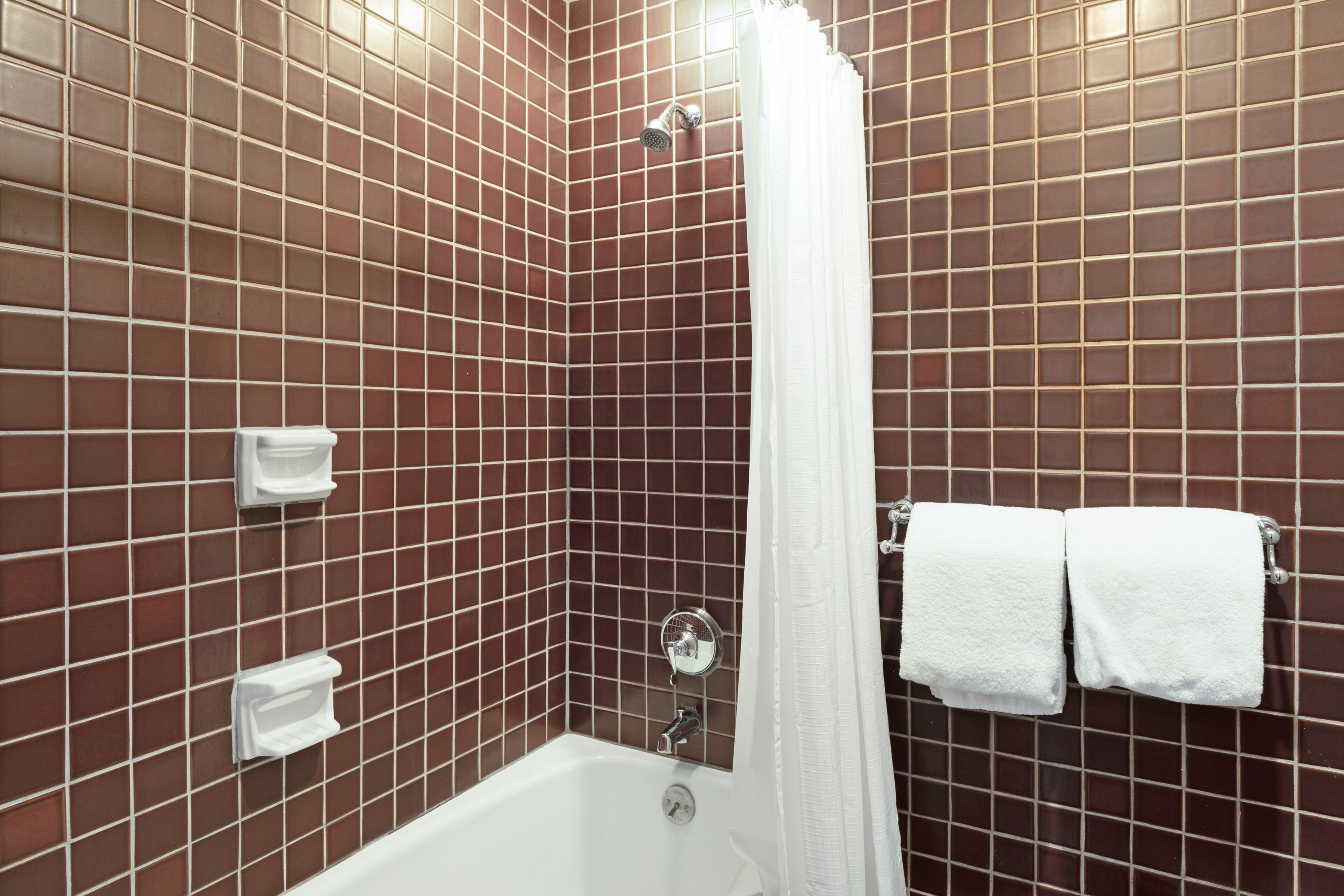 A bathroom with a shower, white tiles, and a towel rack with two towels.