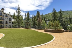 A well-maintained grassy area with a wooden pergola, surrounded by a metal fence and tall evergreen trees. - Charter At Beaver Creek E160 2 Bedroom Condo (Avon)