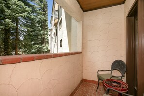 A balcony with a tiled floor, a chair, and a view of a tree and building. - Charter At Beaver Creek E160 2 Bedroom Condo (Avon)