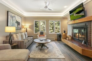 A living room with a fireplace, a ceiling fan, and a television mounted above it. - Charter At Beaver Creek E160 2 Bedroom Condo (Avon)