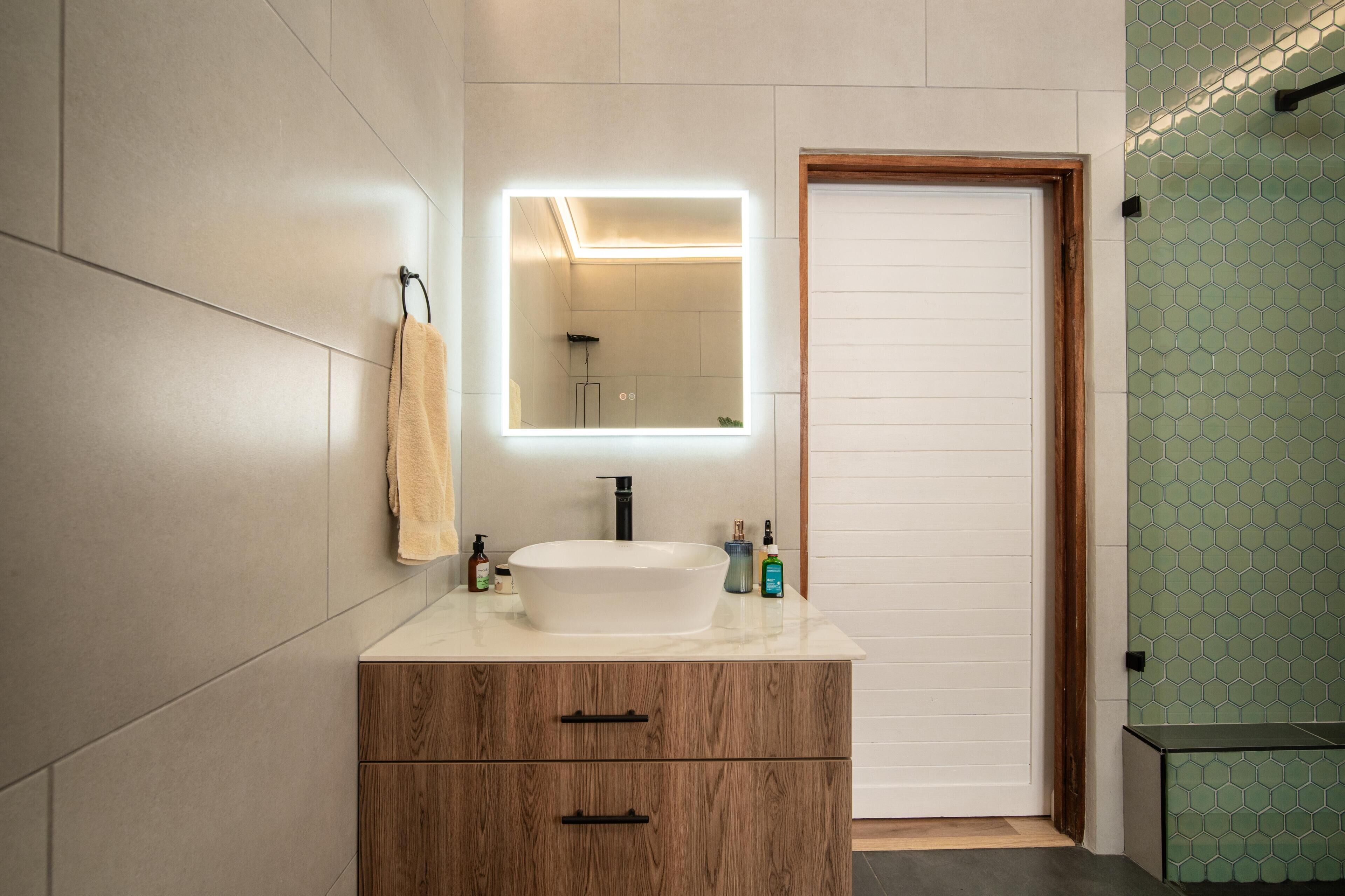Une salle de bain avec un lavabo blanc, un meuble en bois et un miroir avec un éclairage intégré.