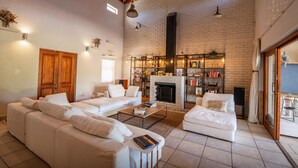 A spacious living room with a white brick fireplace, a large sofa, a coffee table, and a bookshelf filled with books and decorative items. - Spacious 3-bedroom home in Stellenbosch (Stellenbosch)
