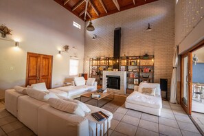 A spacious living room with a white brick fireplace, a large sofa, a coffee table, and a bookshelf filled with books and decorative items. - Spacious 3-bedroom home in Stellenbosch (Stellenbosch)