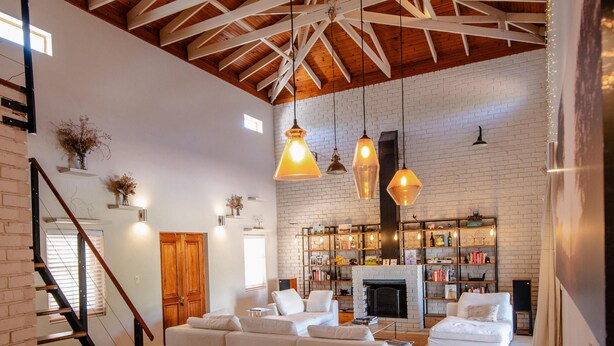 A spacious living area with a wooden ceiling, white brick walls, and a fireplace. There is a dining table with chairs and a staircase leading to another level. - Spacious 3-bedroom home in Stellenbosch (Stellenbosch)