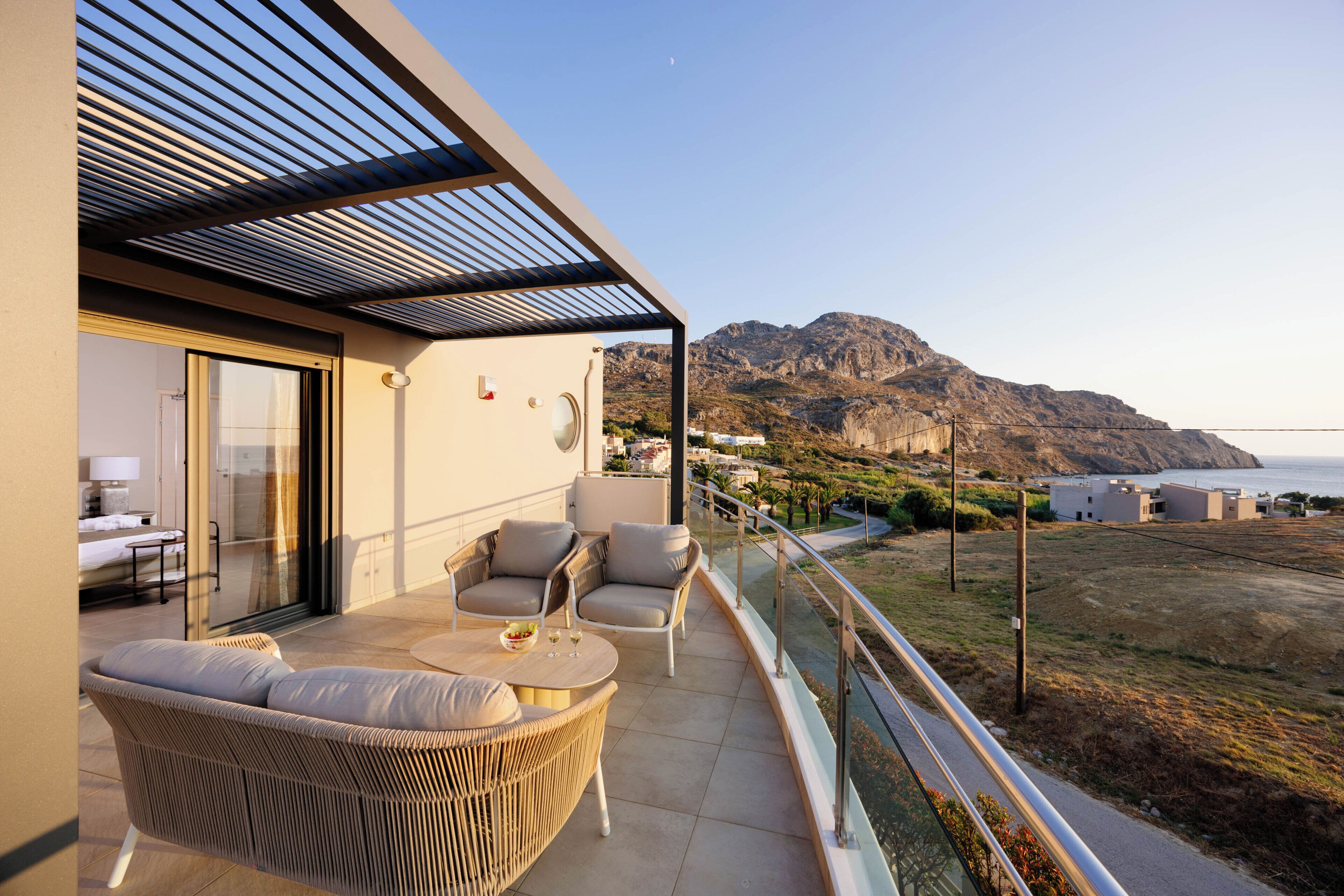 A balcony with wicker furniture, a glass door leading to a room, and a view of a mountainous landscape.