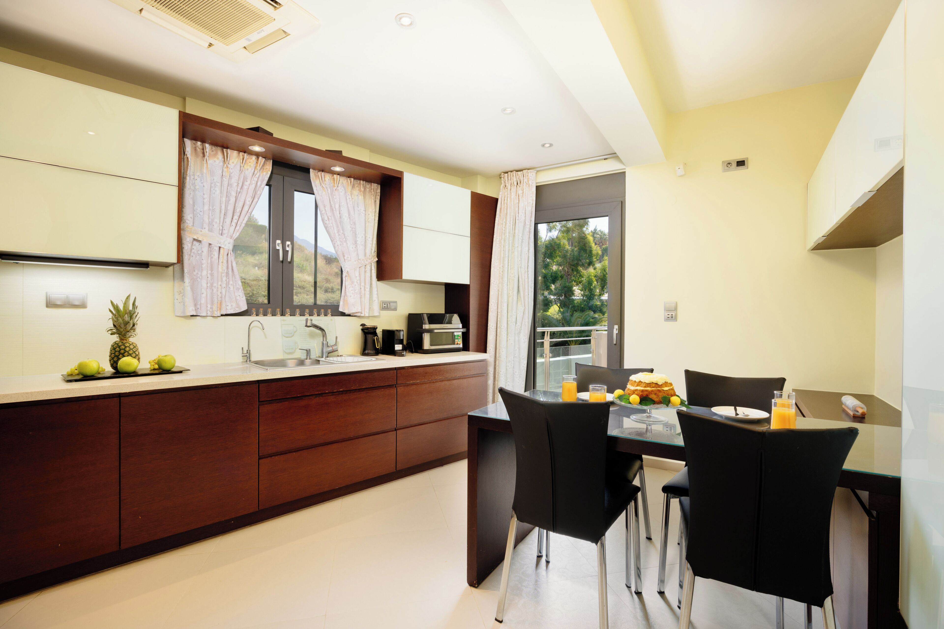 A modern kitchen with a dining area, featuring a large window, a sink, and a dining table with chairs.