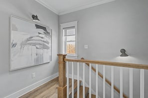 A hallway with a wooden staircase, a large abstract painting, and a window with a view. - Cottages At Lagoon Pass D 2 Bedroom Home (Gulf Shores)