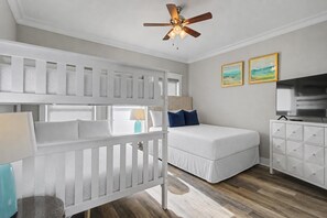 Une chambre avec un lit superposé, un lit simple, un ventilateur de plafond, une télévision et une commode.