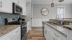 Una cocina moderna con armarios blancos, horno empotrado, microondas y encimera de granito.