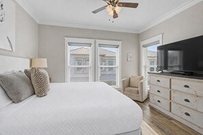 Ein Schlafzimmer mit Bett, Fernseher, Stuhl, Kommode und Deckenventilator.