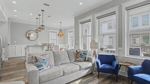 Een ruime woonkamer met een grijze bank, blauwe fauteuils en een houten vloer.