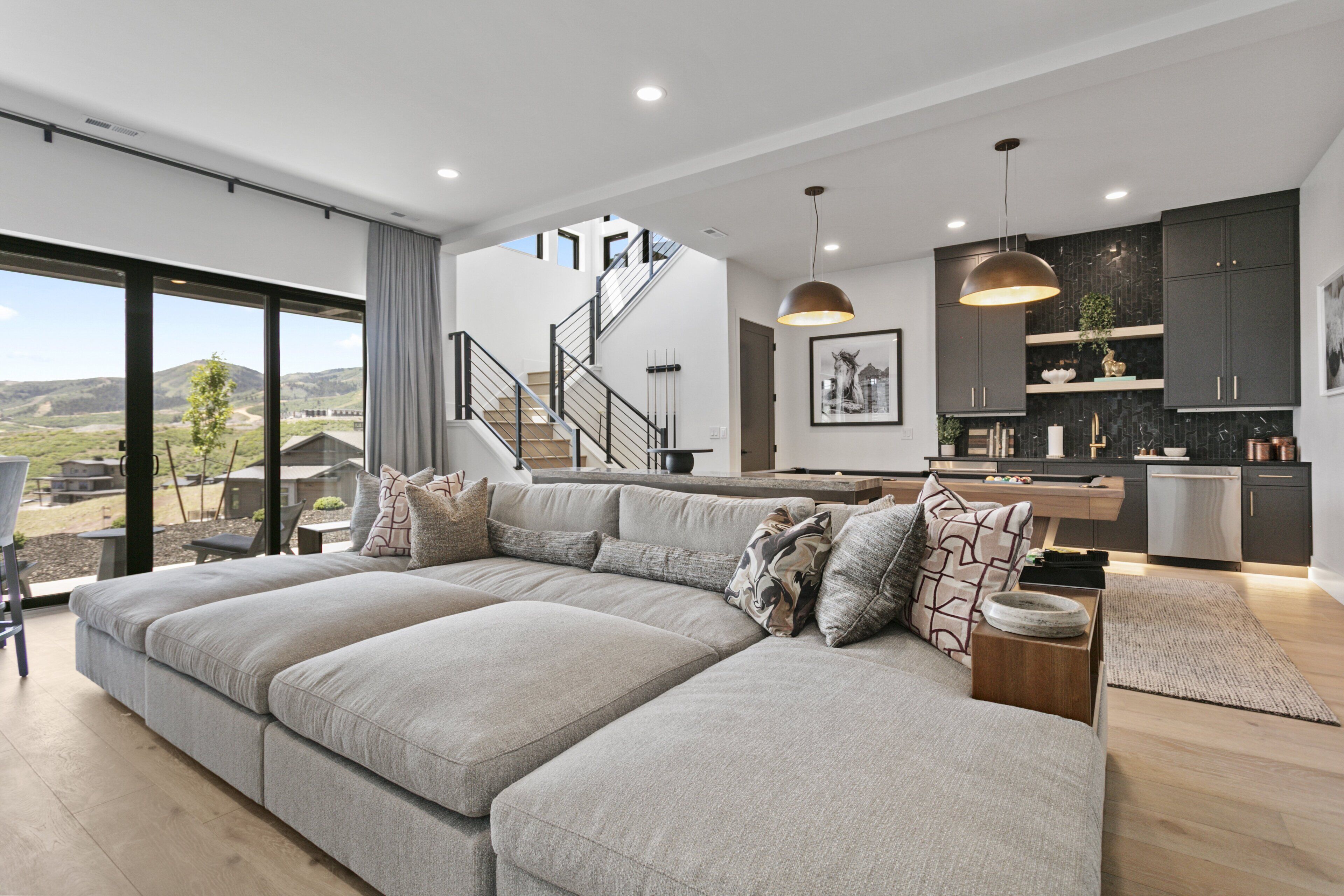 A modern living space with a large sectional sofa, a kitchen area, and a staircase leading to an upper level.