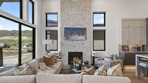 A modern living room with a stone fireplace, a sofa set, and a view of the outdoors. - Mtn Retreat w/ Hot Tub, Game Room & Lake Views (Heber City)