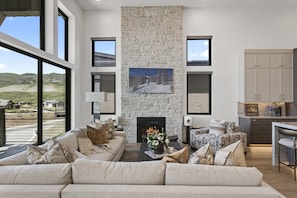 A modern living room with a stone fireplace, a sofa set, and a view of the outdoors. - Mtn Retreat w/ Hot Tub, Game Room & Lake Views (Heber City)