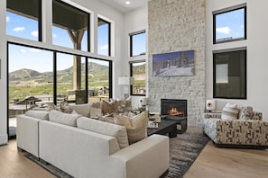 A spacious living room with a fireplace, large windows, and a view of the mountains. - Mtn Retreat w/ Hot Tub, Game Room & Lake Views (Heber City)