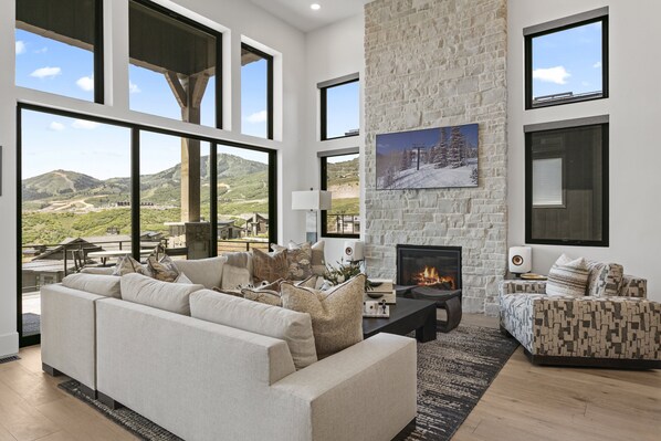 A spacious living room with a fireplace, large windows, and a view of the mountains. - Mtn Retreat w/ Hot Tub, Game Room & Lake Views (Heber City)