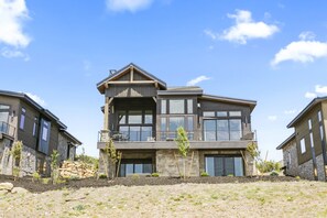 Une maison moderne à deux étages, dotée d’un balcon, de grandes fenêtres et de fondations en pierre.
