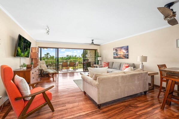 A spacious living room with a large sofa, a dining table, and a TV mounted on the wall. - Big Island Keauhou Punahele C202 2 Bedroom Condo (Kailua-Kona)
