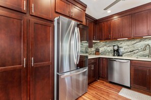 A modern kitchen with wooden cabinets, stainless steel appliances, and a marble backsplash. - Big Island Keauhou Punahele C202 2 Bedroom Condo (Kailua-Kona)
