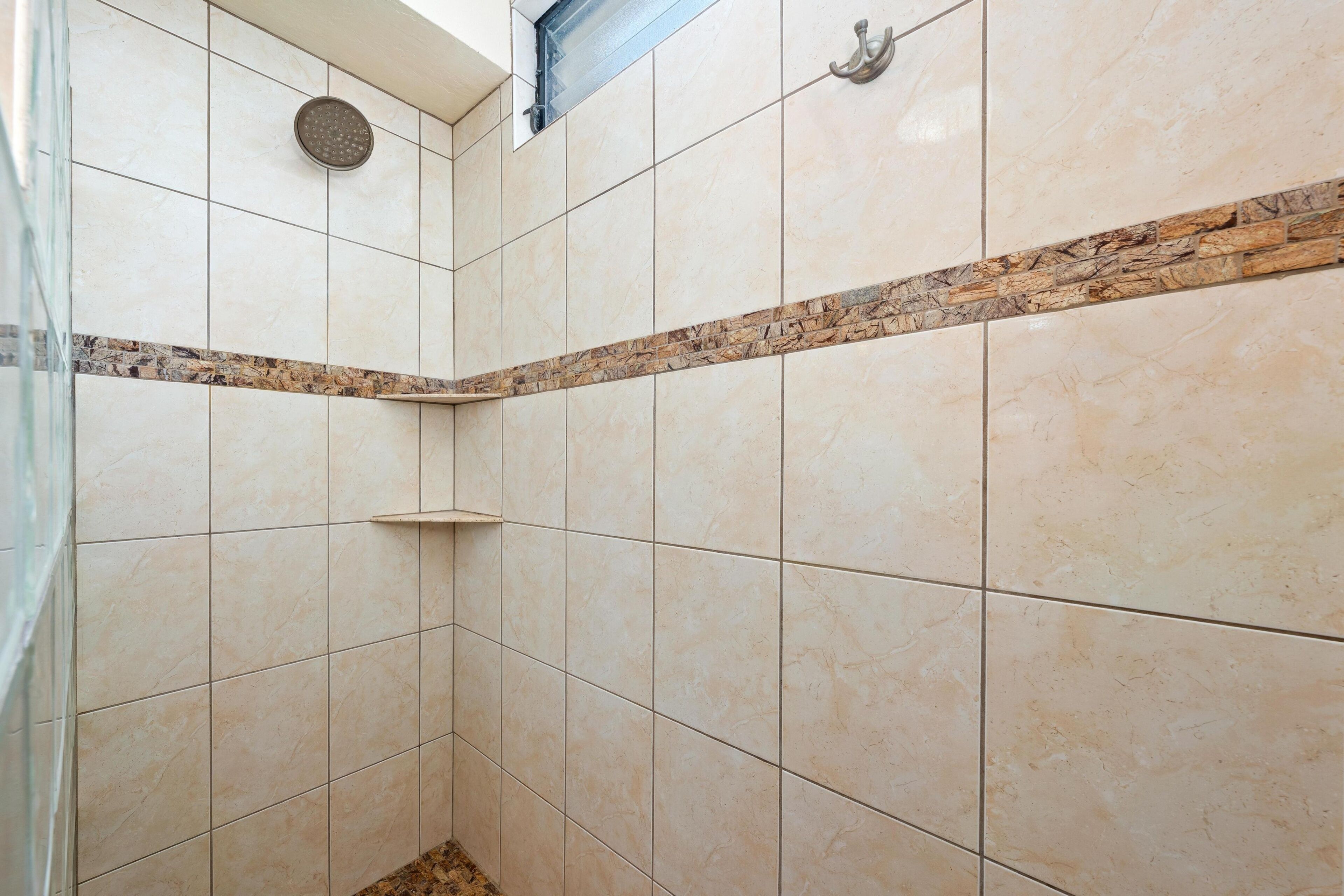 A corner of a bathroom with beige tiles, a showerhead, and a towel rack.