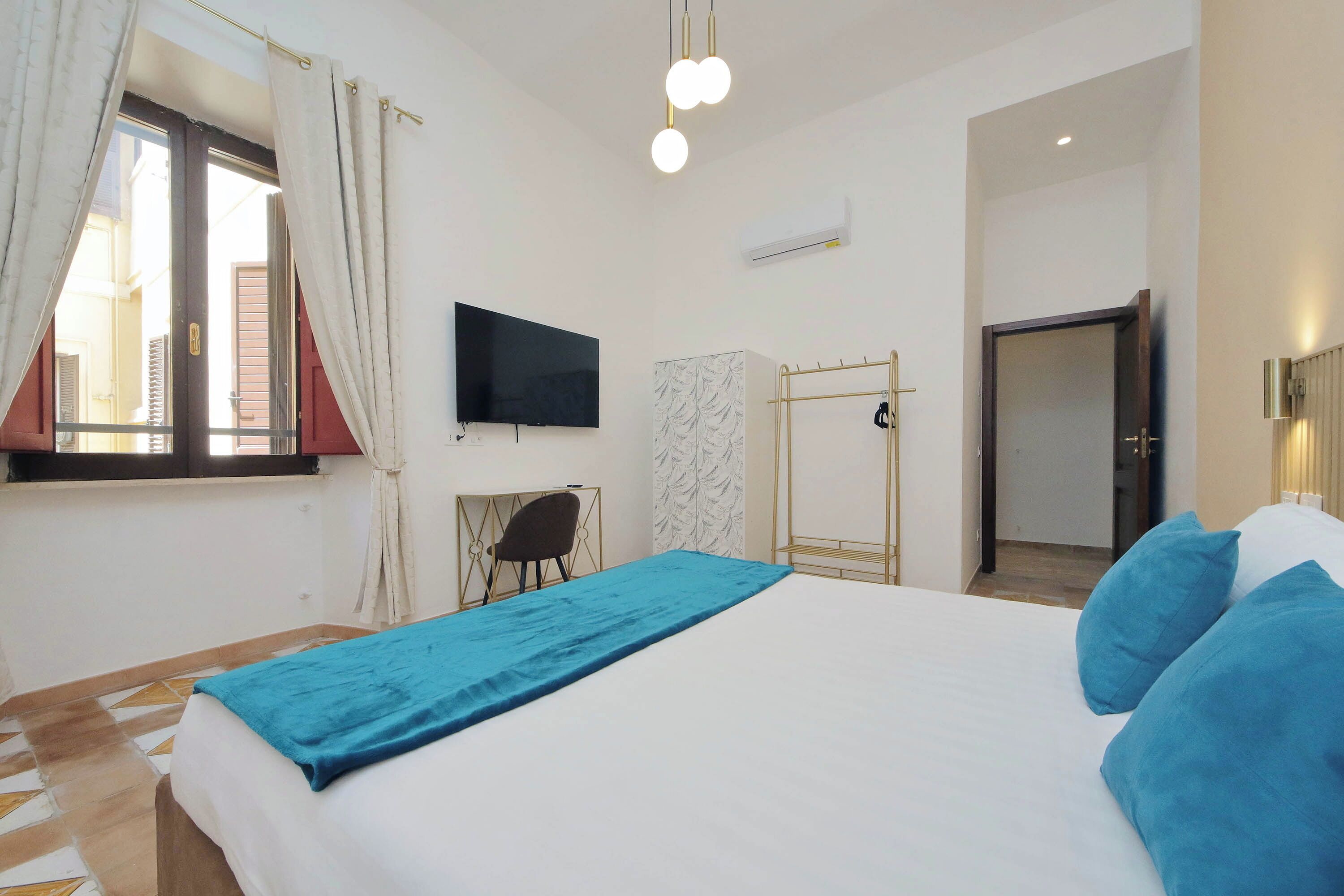 A bedroom with a bed, a TV, a wardrobe, and a window with curtains.