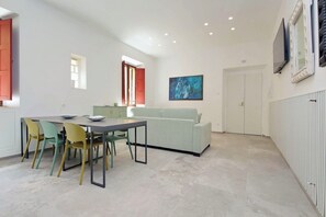 A room with a dining table, chairs, a sofa, a painting, and a window with a view. - Colosseum Grand Luxury Residence for 14 Guests (Roma)