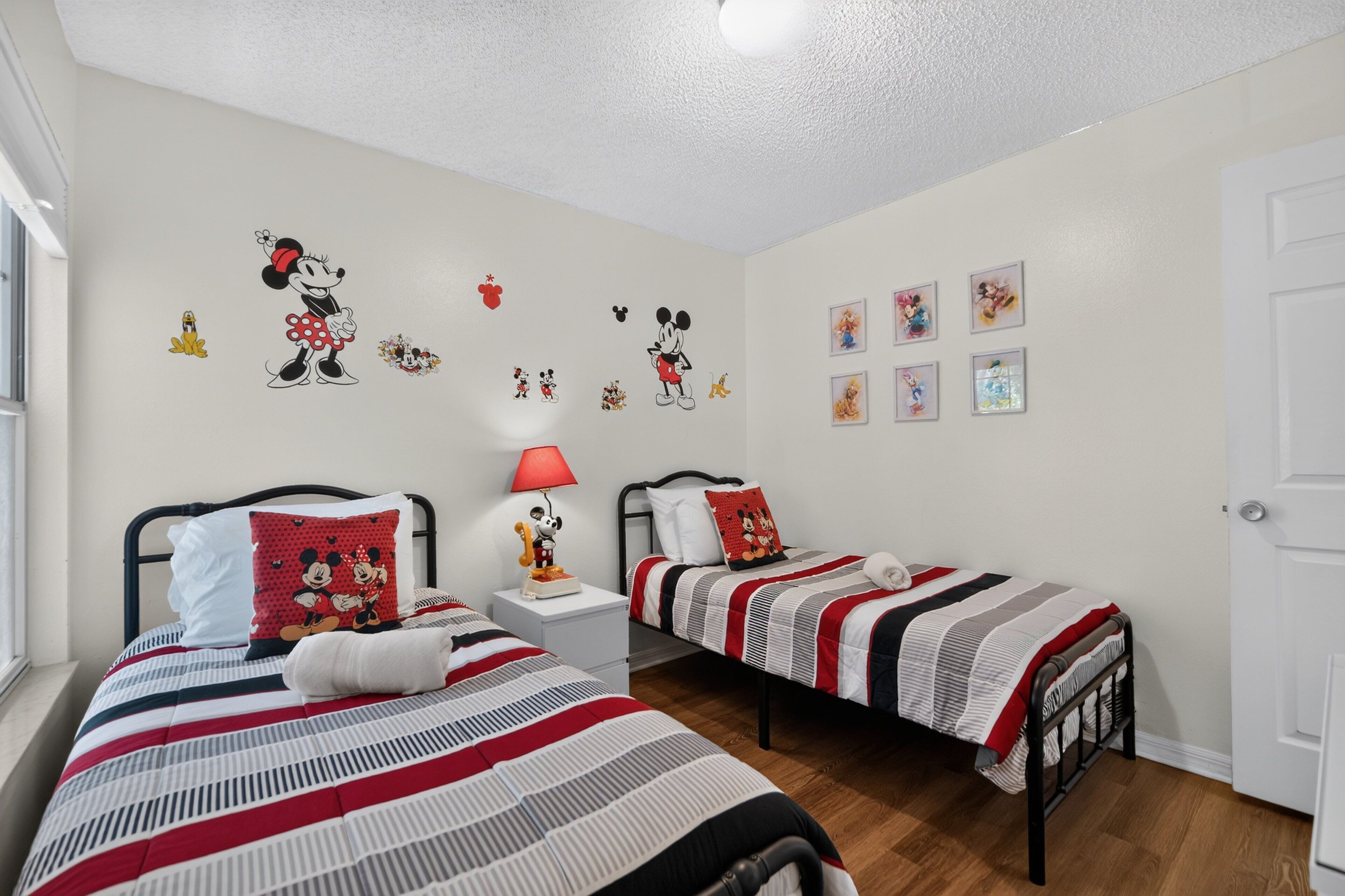 Ein Schlafzimmer mit zwei Betten, jedes mit einem Kissen und Wandbildern zum Thema Mickey Mouse.