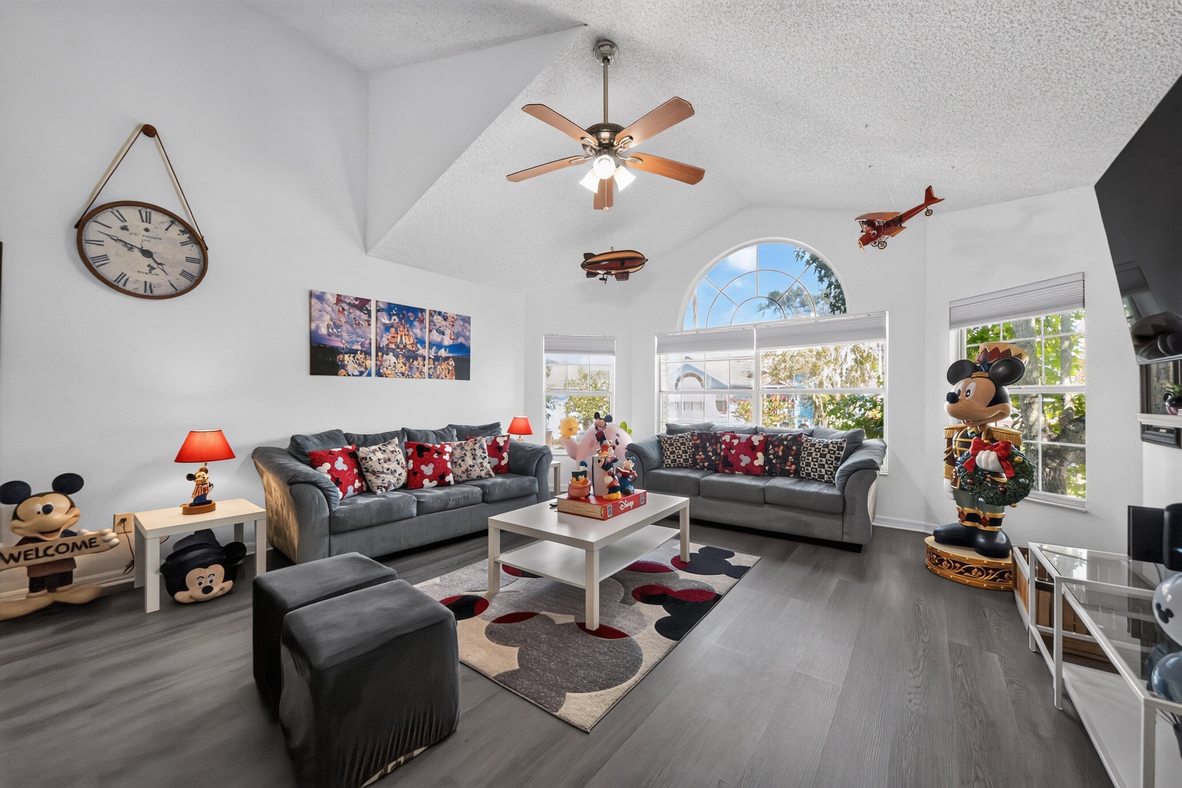 A spacious living room with a ceiling fan, a large window, and a Mickey Mouse statue.
