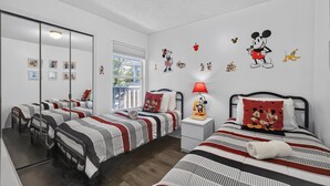 Une chambre d’hôtel avec deux lits, un grand miroir et des décorations à l’effigie de Mickey Mouse sur le mur.