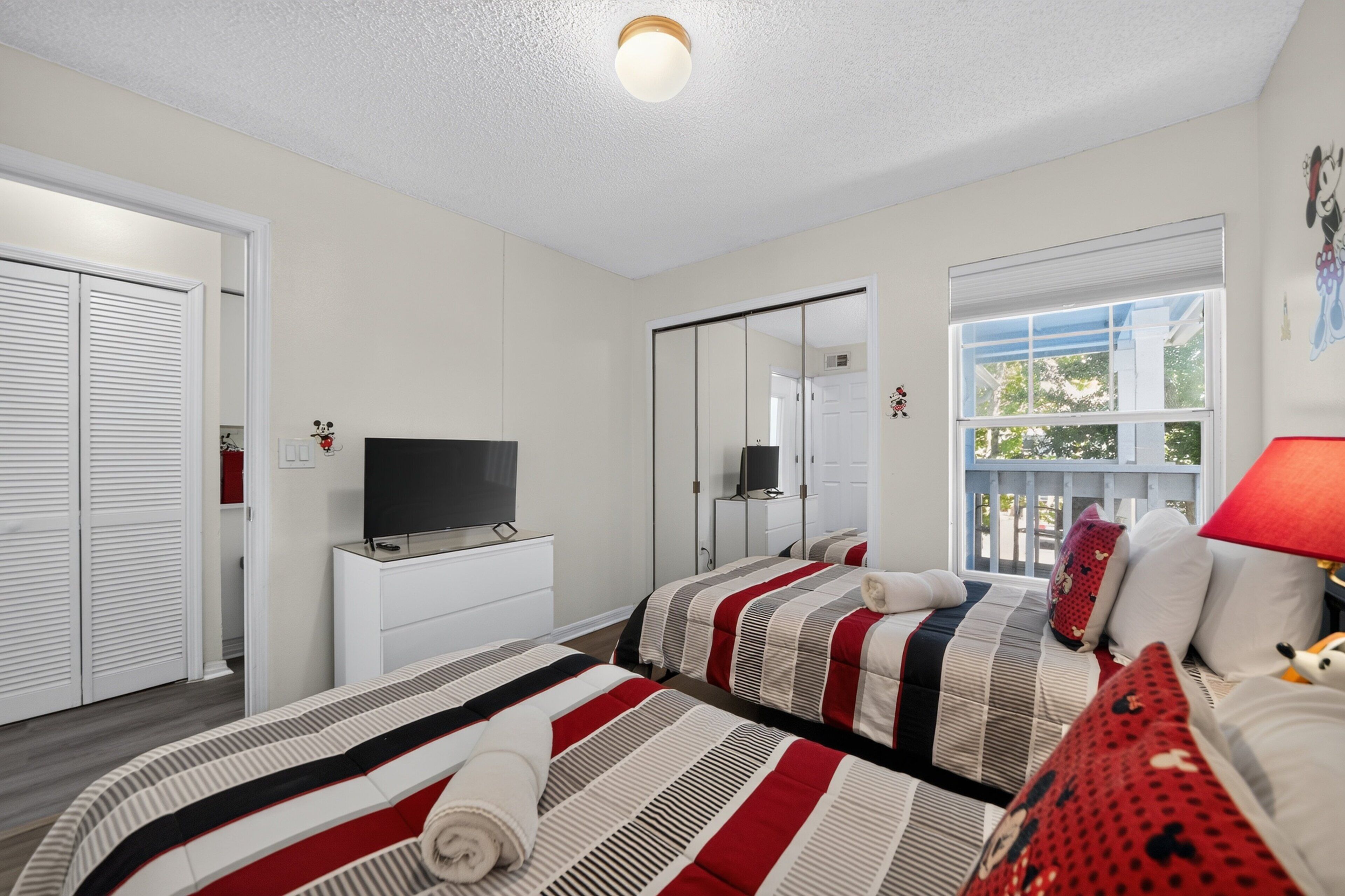 A hotel room with two beds, a television, a mirror, and a window with a view.