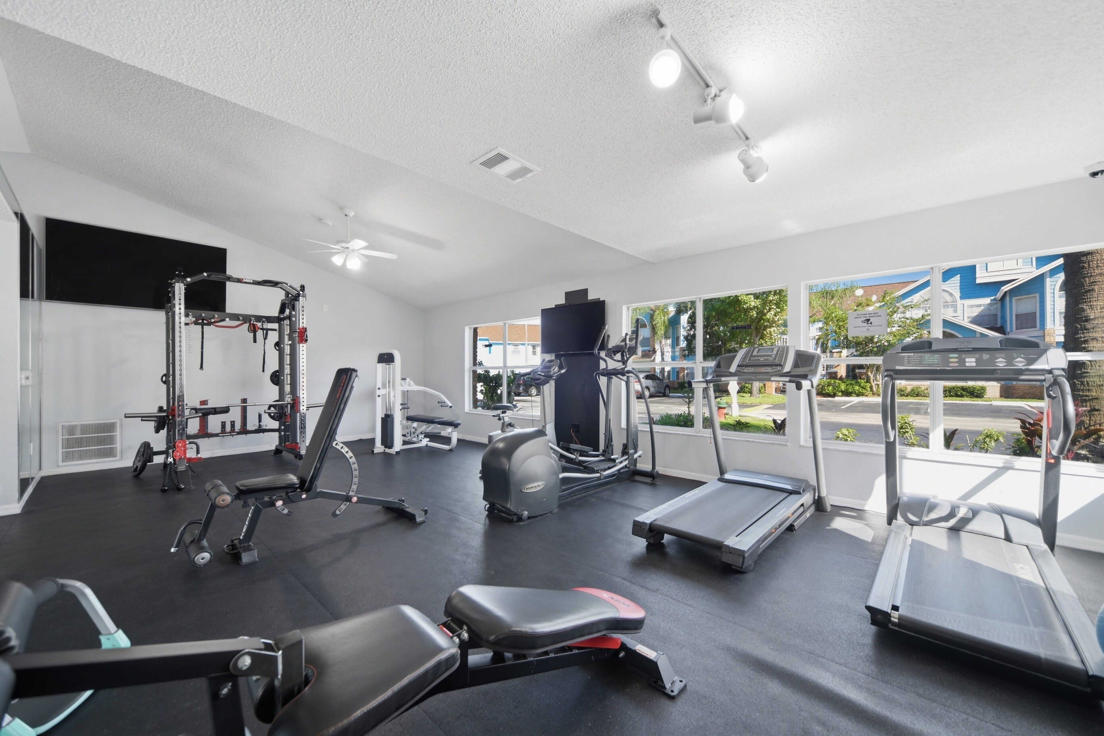 Une salle de sport équipée de divers appareils d’exercice, notamment des tapis de course, un banc de développé couché et des machines de musculation.