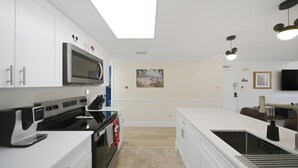A modern kitchen with white cabinetry, a microwave, a stove, and a large island with a sink. - "castle Retreat" Close To All The Magic! 3 Bedroom Condo (Kissimmee)