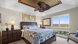 A bedroom with a large bed, two bedside tables, a ceiling fan, and a window with a view. - Golf Villas At Mauna Lani J23 2 Bedroom Condo (Kamuela)