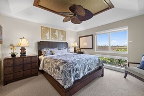 Ein Schlafzimmer mit einem großen Bett, zwei Nachttischen, einem Deckenventilator und einem Fenster mit Blick.