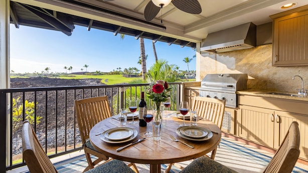 A dining area with a table set for two, a grill, and a view of a golf course. - Golf Villas At Mauna Lani J23 2 Bedroom Condo (Kamuela)