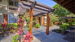 A covered outdoor area with a pergola, potted plants, and a pathway leading to a building. - Golf Villas At Mauna Lani J23 2 Bedroom Condo (Kamuela)